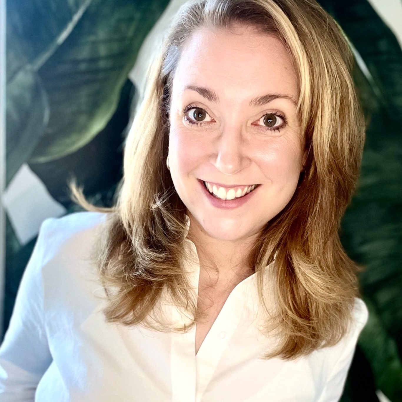 Katharina Henger Eine lächelnde Frau mit langen, hellblonden Haaren vor einem grünen Blatt Hintergrund.