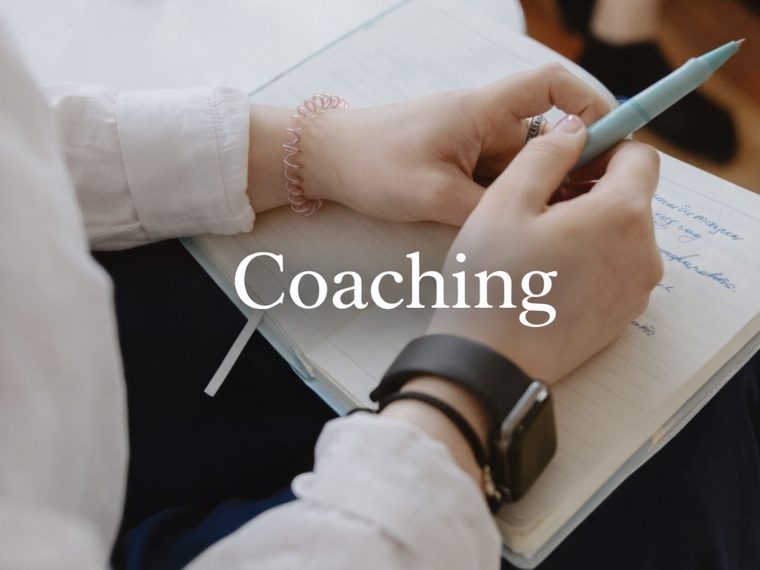 Individuelles Coaching Hände halten einen Stift über einem Notizbuch mit der Aufschrift „Coaching“.